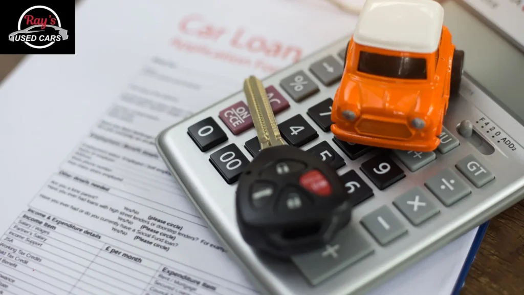 Image of toy car and keys on top of calculator that sits on financial documents